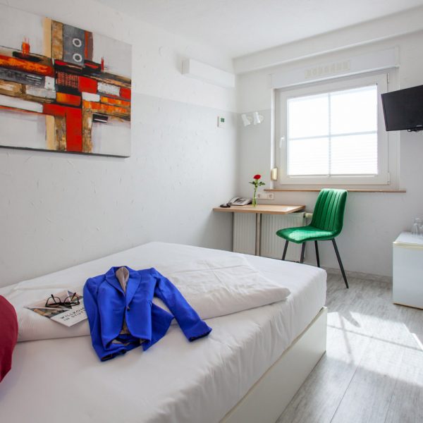 tp-hotelberatung-relax-hotel-micro-einzelzimmer-2 Einzelzimmer mit Bild, Sitzecke, roten Kissen und Jacke auf dem Bett