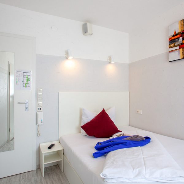 tp-hotelberatung-relax-hotel-micro-einzelzimmer-4 Einzelzimmer mit Bild, roten Kissen und Jacke auf dem Bett
