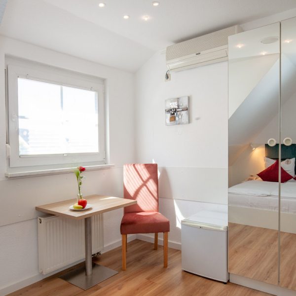 tp-hotelberatung-relax-hotel-standard-doppelzimmer-klima-badewanne-1 Doppelzommer mit Stuhl am Fenster mit Schrank und Rose auf dem Tisch