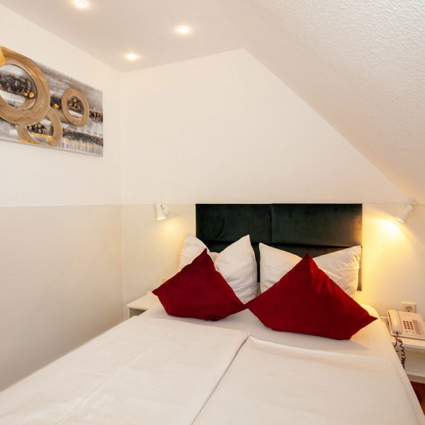 tp-hotelberatung-relax-hotel-standard-doppelzimmer-klima-badewanne-2 Doppelbett mit roten Kissen und Bild an der Wand